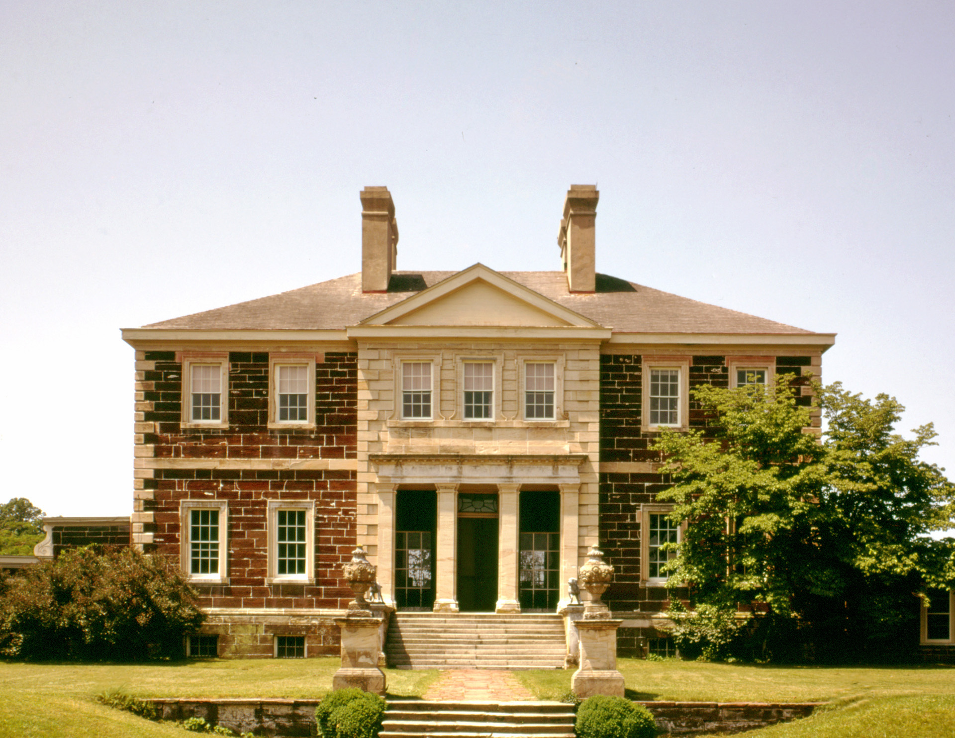 Palladian style house features nearly perfect symmetry, brick walls, window mouldings, cornice mouldings, and a covered entrance with columns.