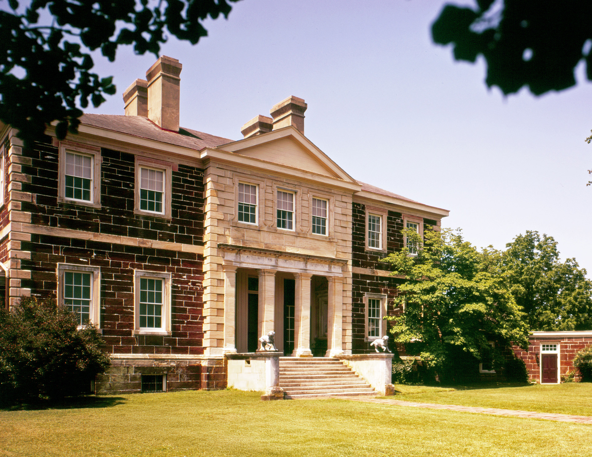 A side angle of a palladian style house featuring perfect symmetry, brick walls, window mouldings, cornice mouldings, and a covered entrance.